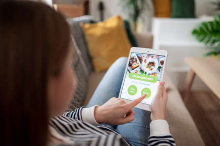 Young woman with tablet ordering food at home, coronavirus and food delivery concept.