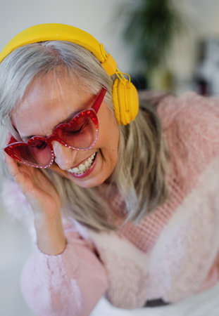 Portrait of senior woman with sunglasses and headphones indoors at home, laughing.