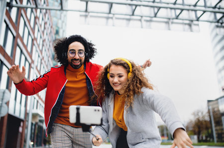 Young couple with smartphone making video for social media outdoors on street.の写真素材