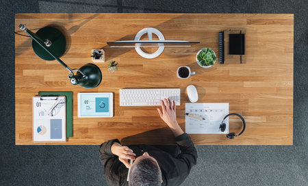 Top view of businessman working on computer at desk with paperwork in home office.の写真素材