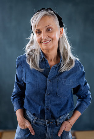Portrait of senior woman standing indoors against dark background, standing.