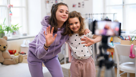 Sisters indoors at home, making video with smartphone. Lockdown concept.