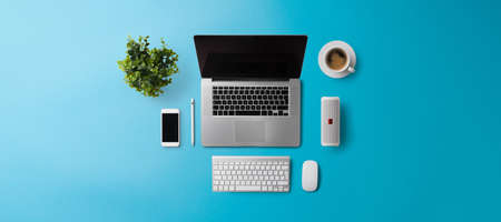 Flat lay top view office desk working space with laptop on blue background. Copy space.