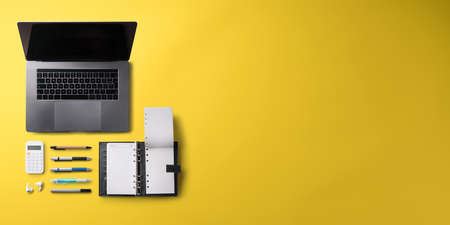 Flat lay top view office desk working space with laptop on yellow background. Copy space.の写真素材