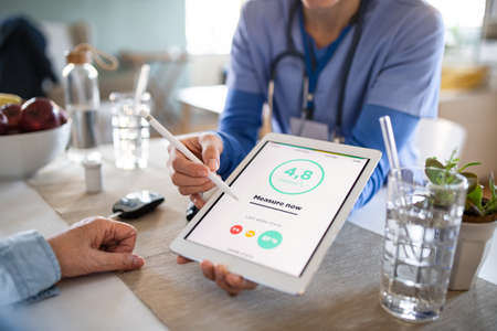 Caregiver or healthcare worker with senior woman patient, measuring blood glucose indoors.