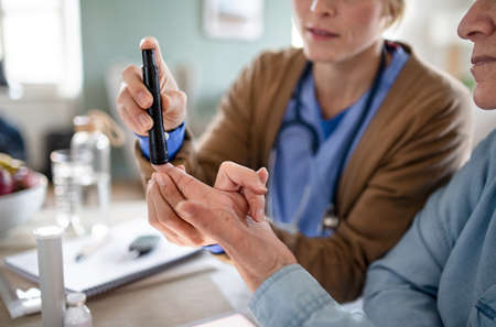 Midsection of caregiver or healthcare worker with senior woman patient, measuring blood glucose indoors.の写真素材