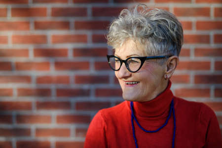 Senior woman standing outdoors against brick wall background. Copy space.の写真素材