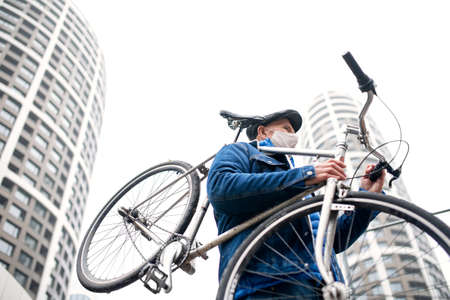 Senior man carrying bicycle outdoors on street in city, coronavirus concept.の写真素材