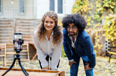 Young couple with smartphone making video for social media outdoors in park.の写真素材