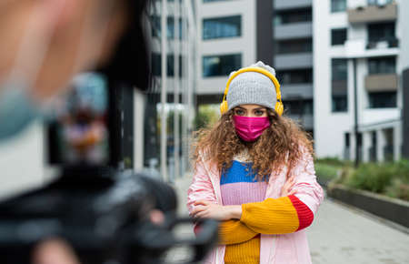 Young woman with headphones making video for social media outdoors on street, coronavirus concept.の写真素材