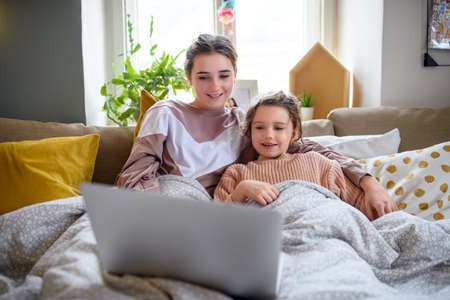 Sisters indoors at home, using laptop. Lockdown concept.