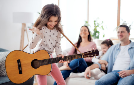 Small girl with family indoors at home, having fun with guitar.の写真素材