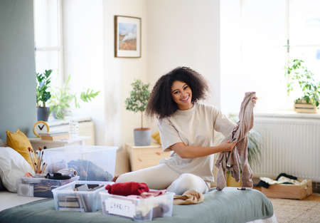 Young woman sorting clothing indoors at home, charity donation concept.の写真素材