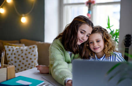 Sisters schoolgirls with laptop learning online indoors at home,  concept.の写真素材