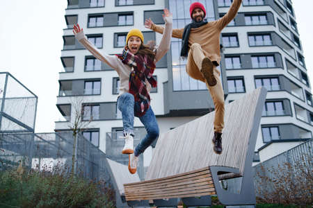 Cheerful young couple owners jumping outdoors in front of new flat, new home and relocation concept.