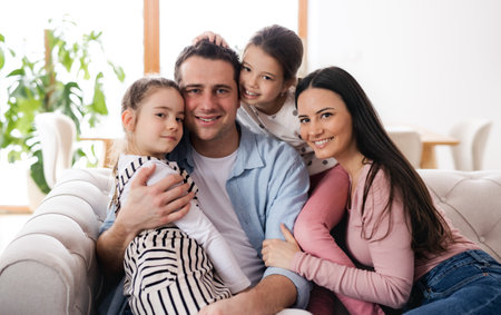 Parents with small daughters sitting on sofa indoors at home, looking at camera.