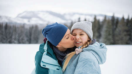 Mother kissing small daughter outdoors in winter nature, Tatra mountains Slovakia.の写真素材