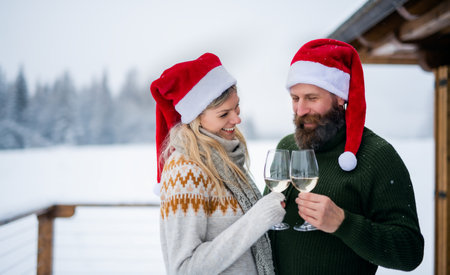 Happy couple drinking wine on terrace outdoors in winter nature, holiday at Christmas time.の写真素材
