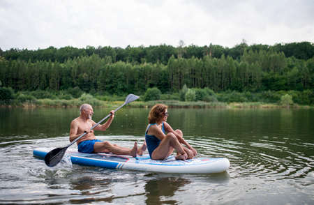 Senior couple paddleboarding on lake in summer.の写真素材