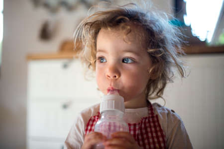 Small girl indoors in kitchen at home, drinking milk from bottle.の写真素材