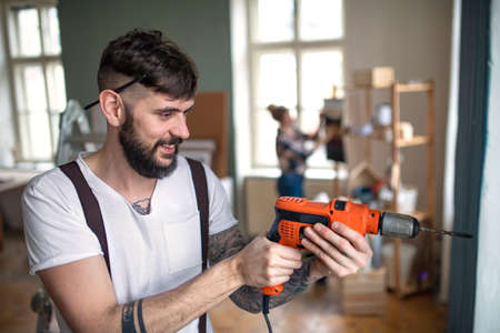 Man with drill working indoors at home, relocation and diy concept.