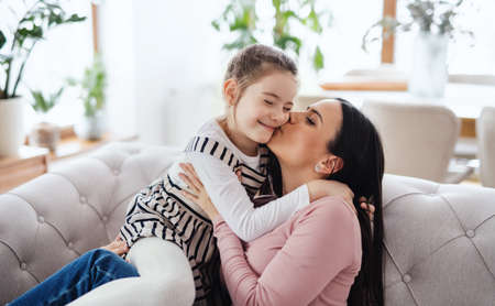 Mother with small daughter sitting on sofa indoors at home, kissing.