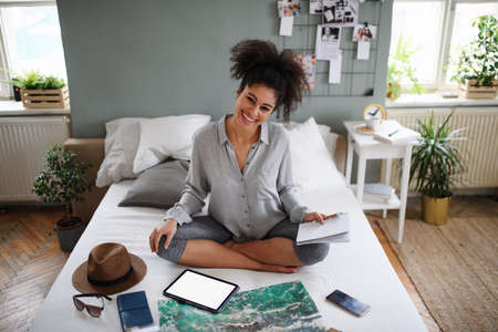 Young woman with tablet and map indoors at home, planning traveling trip.の写真素材