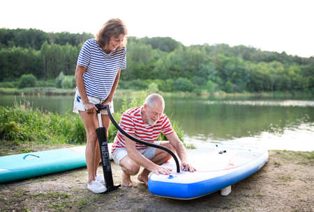 Senior couple getting ready for paddleboarding by lake in summer.の写真素材