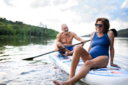 Senior couple paddleboarding on lake in summer.の写真素材
