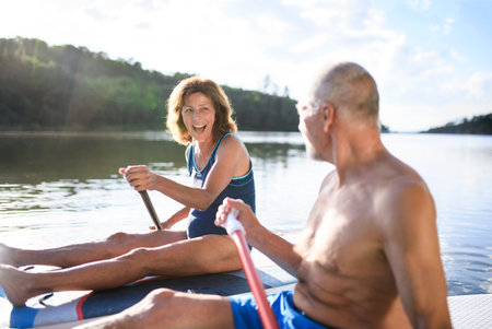Senior couple paddleboarding on lake in summer.の写真素材