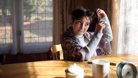 Poor sad small girl cutting hair indoors at home, poverty concept.の写真素材
