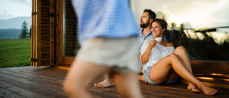 Family with small daughter sitting on patio of wooden cabin, holiday in nature concept.の写真素材
