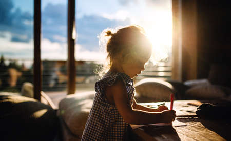 Small girl drawing pictures in wooden cabin, holiday in nature concept.