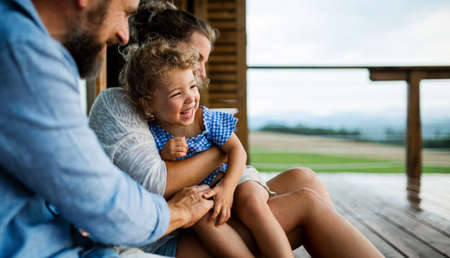 Family with small daughter sitting on patio of wooden cabin, holiday in nature concept.の写真素材
