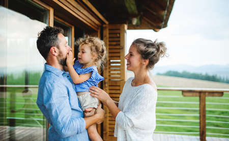 Family with small daughter on patio of wooden cabin, holiday in nature concept.