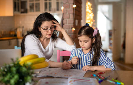 Mother with small daughter in kitchen, home schooling and distance learning concept.の写真素材