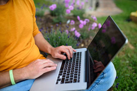 Unrecognizable man with laptop working outdoors in garden, home office concept.の写真素材