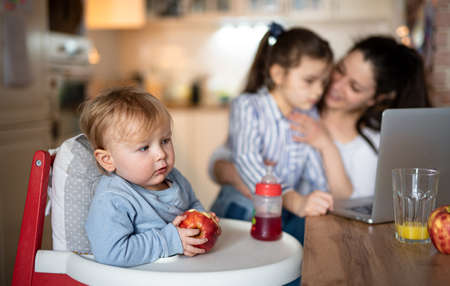 Small toddler girl with mother and sister, sitting in highchair.の写真素材