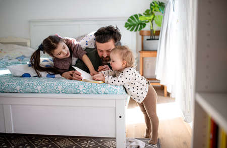 Father with two small daughters having fun on bed at home.の写真素材