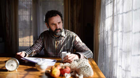 Portrait of unhappy poor mature man reading newspapers indoors at home, poverty concept.の写真素材
