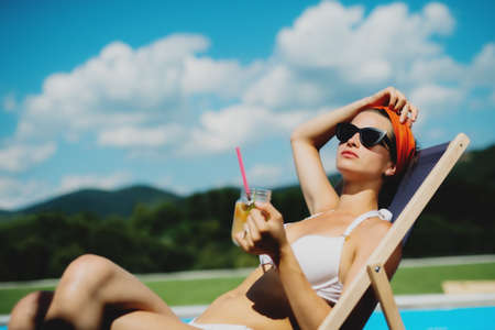 Young woman sitting by swimming pool outdoors in backyard garden, relaxing.