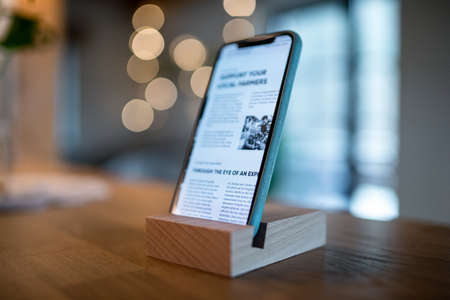 Smartphone in wooden stand holder on table indoors at home or on office.
