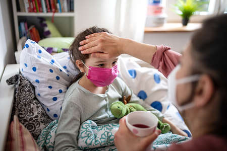 Mother looking after sick small daughter in bed at home, coronavirus concept.の写真素材