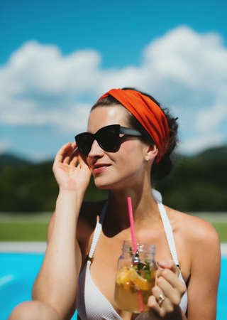 Young woman sitting by swimming pool outdoors in backyard garden, relaxing.の写真素材