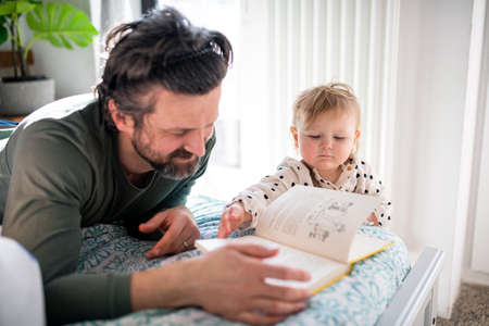 Father with small daughter reading book indoors at home.