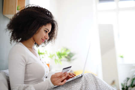 Portrait of young woman with laptop indoors on bed, online shopping concept.の写真素材