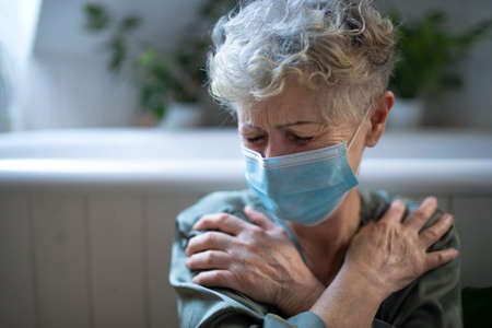 Depressed senior woman with face mask at home,   mental health concept.の写真素材