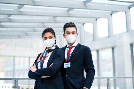 Young flight attendants looking at camera in airport lounge, travel and new normal.