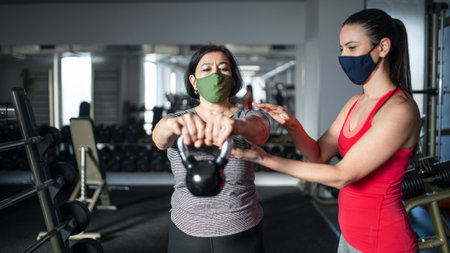 Senior woman with personal trainer doing exercise in gym