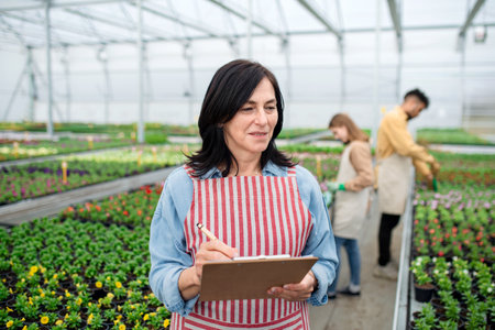 Senior woman with clipboard in greenhouse in garden center, working.の写真素材